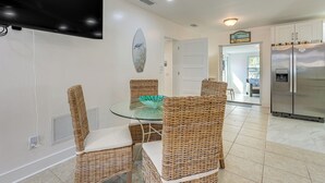 A modern kitchen with a large refrigerator, a dining table with wicker chairs, and a flat-screen TV mounted on the wall. - Clearwater Beach Home w/ Private Pool & Pool Table (Clearwater)