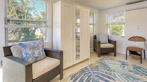A room with a wicker sofa, a white wardrobe, a wicker chair, and a view of palm trees through the windows. - Clearwater Beach Home w/ Private Pool & Pool Table (Clearwater)