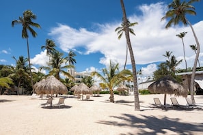A beach with palm trees, thatched umbrellas, and lounge chairs. - Premium 2 Bedrooms Panoramic Beach View Condo (Punta Cana)