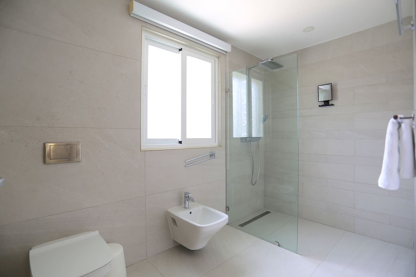 A modern bathroom with a glass-enclosed shower, a toilet, a sink, and a window.