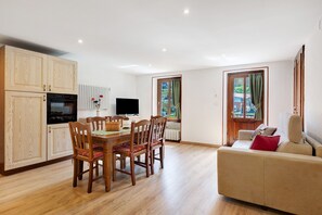 Eine moderne Küche mit Holzschränken, einem Esstisch mit Stühlen, einer Couch und einem Fernseher.