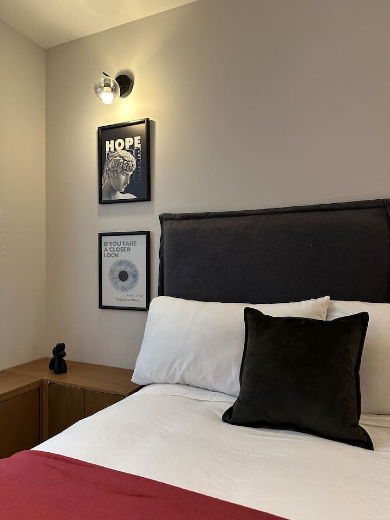 Un lit bien fait, avec une literie blanche et noire, une tête de lit sombre et deux tableaux encadrés accrochés au mur.