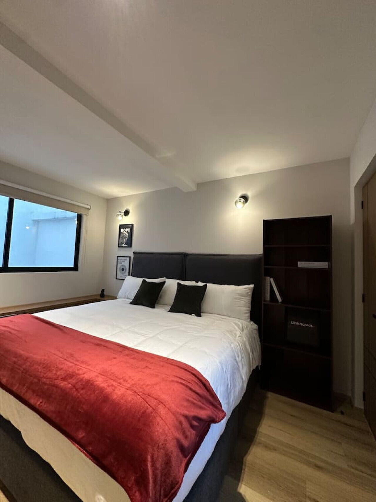 A modern bedroom with a large bed, a dark headboard, and a wooden wardrobe.