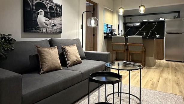 A modern living room with a grey sofa, two black side tables, and a large painting of a bridge and seagull. - Departamento Moderno Soho POP 104 Narvarte (Mexico City)