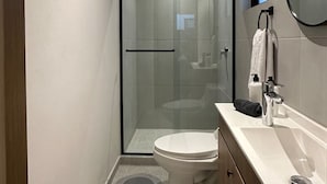A modern bathroom with a glass-enclosed shower, a toilet, and a vanity with a mirror. - Departamento Moderno Soho POP 104 Narvarte (Mexico City)