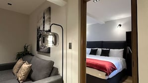 A modern room with a grey sofa, a bed with a red and white duvet, and a wall-mounted light fixture. - Departamento Moderno Soho POP 104 Narvarte (Mexico City)