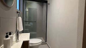Un bagno moderno con cabina doccia in vetro, un water bianco e un mobile lavabo con uno specchio e due flaconi di sapone.