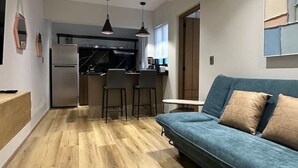 Un soggiorno moderno con un divano blu, pavimento in legno e una cucina sullo sfondo.