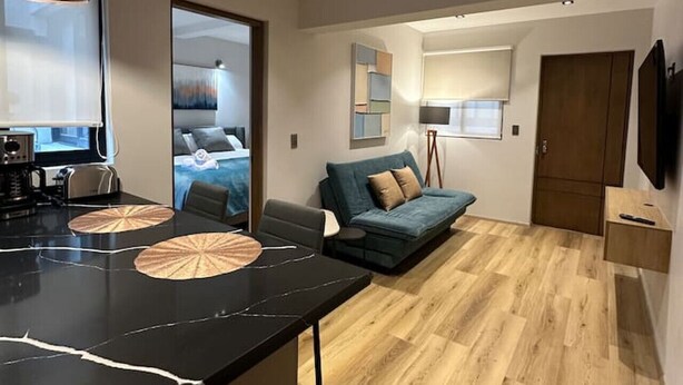 Una cucina moderna con un piano di lavoro in marmo nero, una zona pranzo con tavolo nero e un soggiorno con divano blu e pavimento in legno.