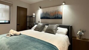 Una camera da letto moderna con un grande letto, un quadro astratto appeso al muro e un comodino con un vaso di fiori.