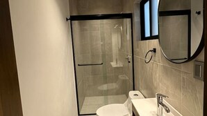 A modern bathroom with a glass-enclosed shower, a toilet, a sink with a mirror, and a ceiling light. - Departamento  Boutique en Narvarte  204 (Mexico City)