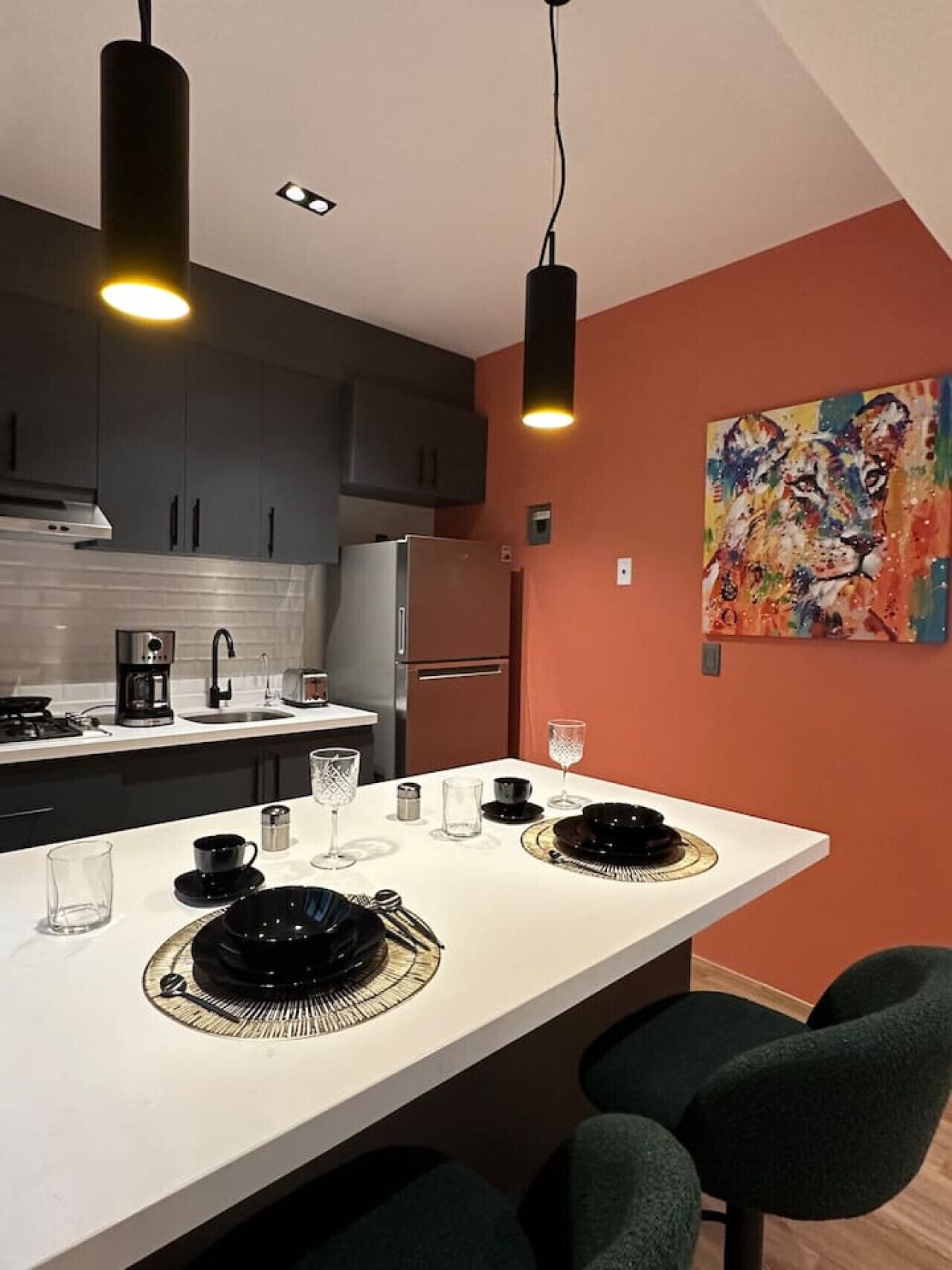 A modern kitchen with dark cabinets, a white countertop, and a dining area with a white table set for two.