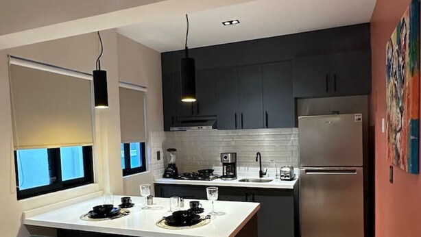 A modern kitchen with dark cabinets, a stainless steel refrigerator, and a dining area with two chairs. - Departamento  Boutique en Narvarte  204 (Mexico City)