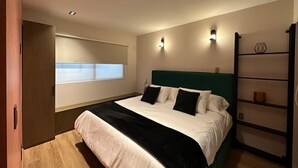 A modern bedroom with a large bed, a built-in shelf, and a window with blinds. - Departamento  Boutique en Narvarte  204 (Mexico City)
