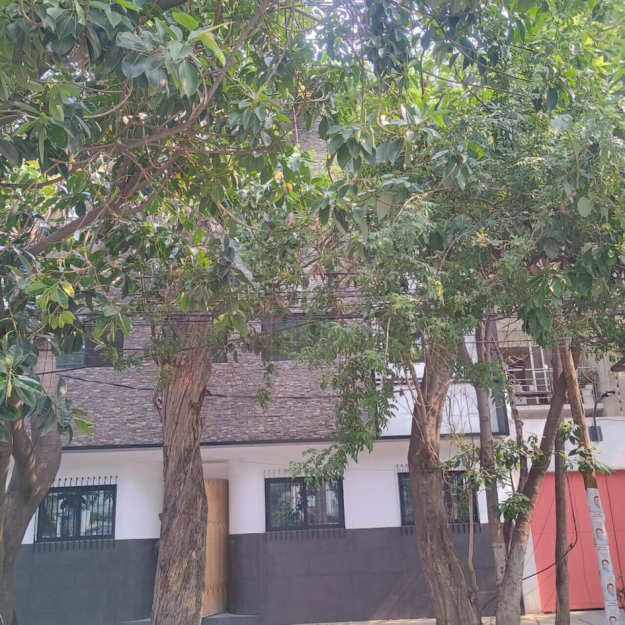 Un bâtiment à la façade blanche, dont la partie inférieure est noire, et qui possède une porte rouge. Des arbres se trouvent devant le bâtiment.