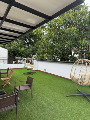 An outdoor patio with artificial grass, wicker chairs, and a hanging chair. - Elegante Departamento New England 202 Narvarte (Mexico City)