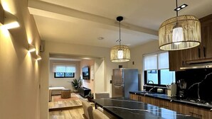 A modern kitchen with a long island, bar stools, pendant lighting, and wooden cabinets.