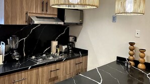 A modern kitchen with wooden cabinets, black marble countertops, and two hanging pendant lights.
