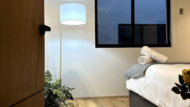 Ein Schlafzimmer mit einem Bett, einem Nachttisch, einer Stehlampe und einem Fenster.