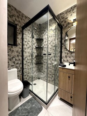 Ein modernes Badezimmer mit einer Duschkabine, einer Toilette, einem Waschbecken mit Spiegel und Fliesen mit Muster.