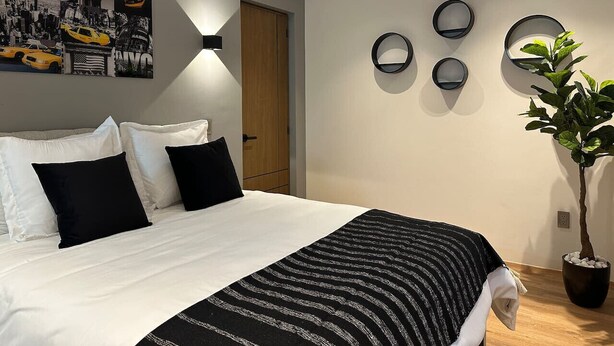Une chambre avec un lit, des oreillers noirs et blancs, une couverture rayée noire et blanche, un mur orné de miroirs ronds et une plante en pot.