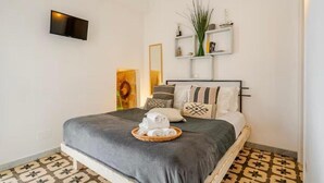 A neatly arranged bedroom with a bed, a flat-screen TV mounted on the wall, and a small shelf with decorative items. - NAP25GUESTHOUSE (Polignano a Mare)
