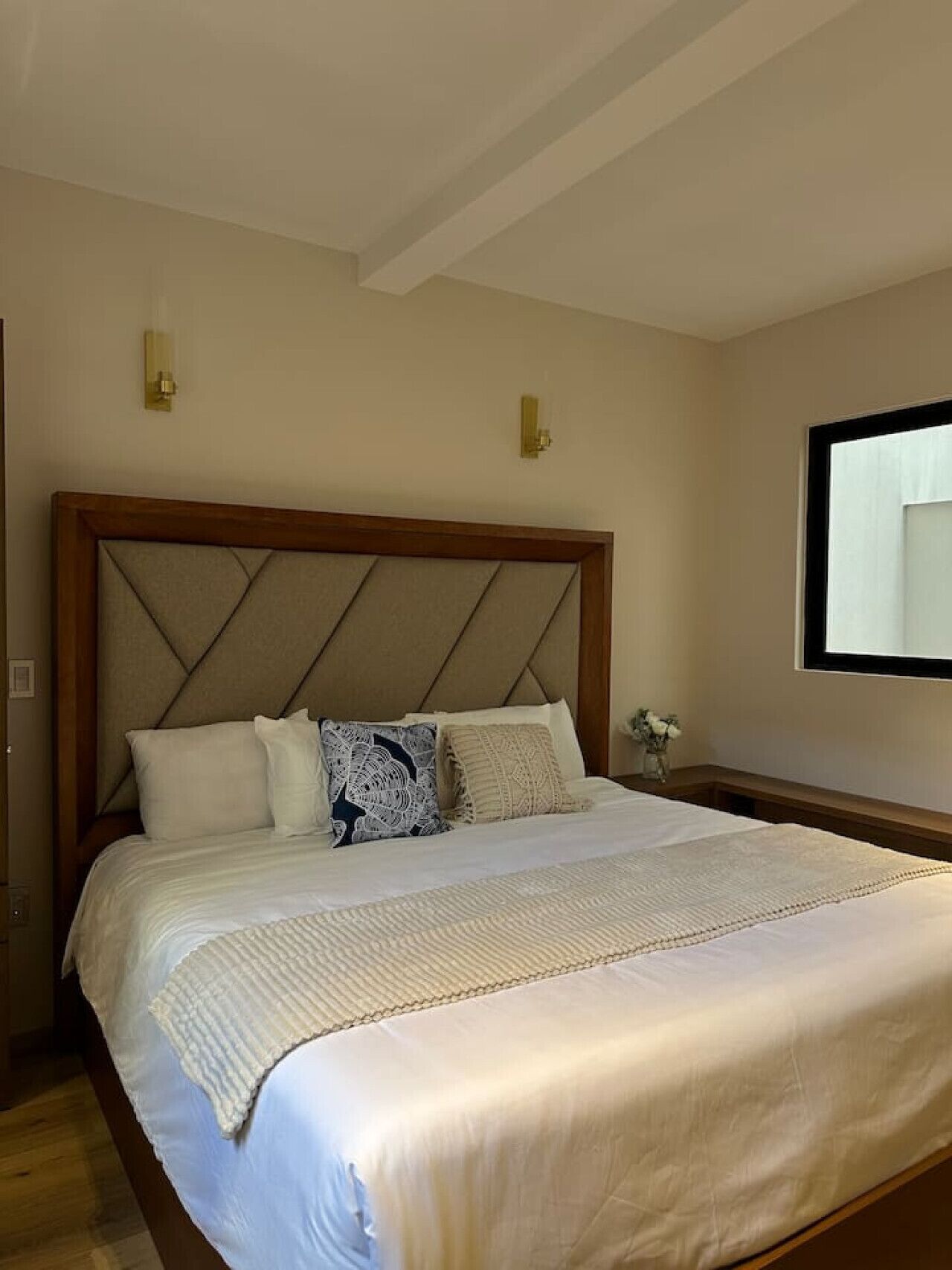 Ein Schlafzimmer mit einem großen Bett, einem hölzernen Kopfteil, zwei Wandleuchten und einem Fenster mit Blick.