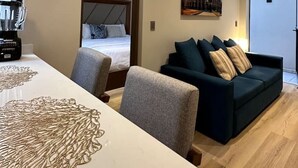 Moderni hotellihuone, jossa on sänky, sohva, ruokapöytä ja Colosseum-aiheinen taulu.