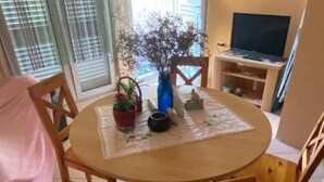 Ett runt träbord med en bordsduk, omgivet av trästolar. På bordet står en krukväxt, en liten vas och en kopp.