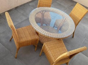 Une table ronde en verre, entourée de chaises en osier, sur une terrasse carrelée.