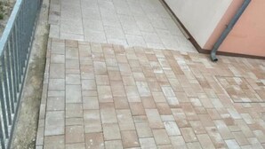 En asfalterad gångväg med ett fiskbensmönster, avgränsad av ett metallräcke och en låg mur.