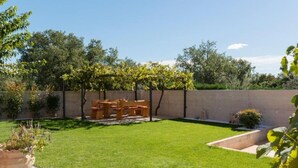 A backyard with a wooden bench and table set, a small garden area with plants, and a low stone wall. - Comfort Villa Roza in Umag - 5 Bedroom With Pool (Umag)