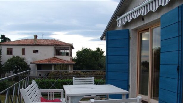 A patio with white furniture, a blue door, and a building with a tiled roof in the background. - One Bedroom Apartment with Terrace (Savudrija)