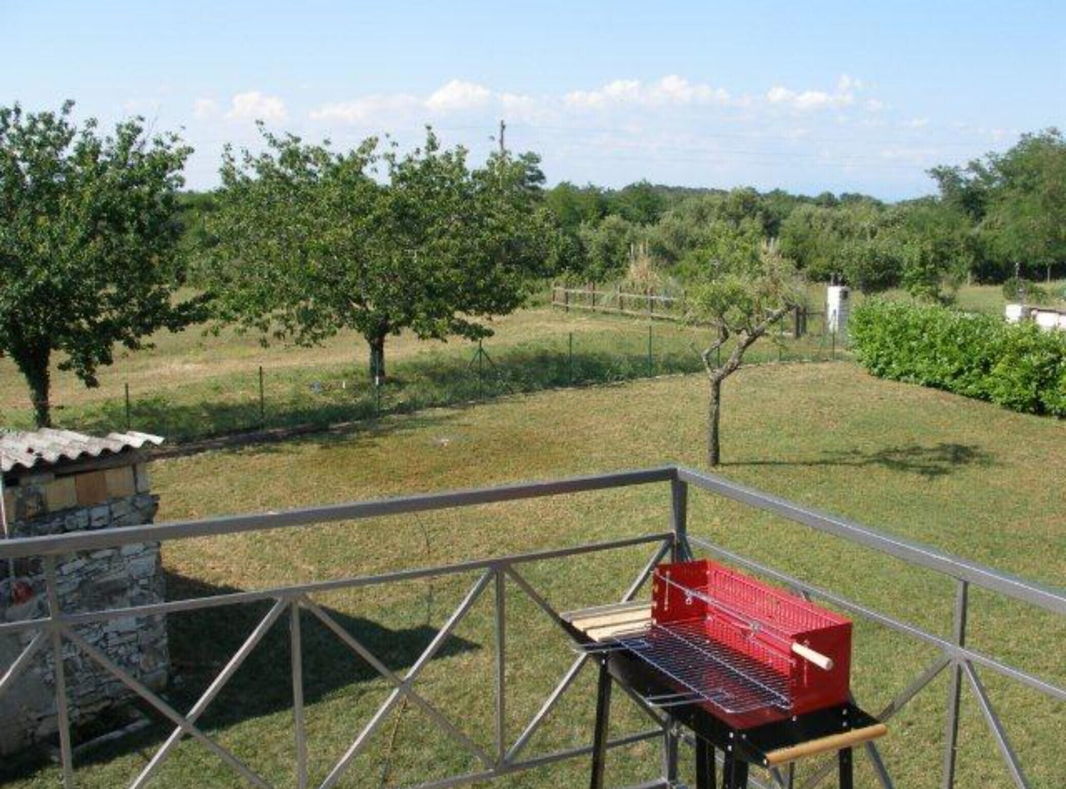 A patio area with a metal railing, a stone structure, and a red grill.