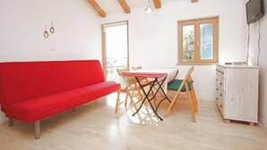 A room with a red sofa, a wooden dining table with chairs, a white cabinet, and a television on the wall. - One Bedroom Apartment with Terrace (Savudrija)