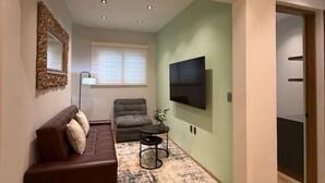 Ein modernes Wohnzimmer mit einem braunen Sofa, einem grauen Sessel, einem kleinen runden Tisch und einem flachbildfernseher an der Wand.