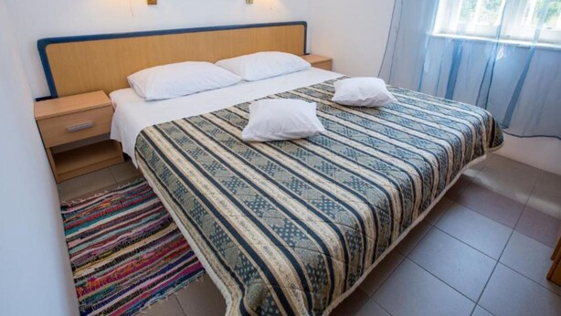 A neatly made bed with a patterned bedspread, two bedside lamps, a wall art of butterflies, and a window with curtains. - Mediterraneo Goga Apartments - TwoBedroom Apartment With Terrace (Mali Losinj)