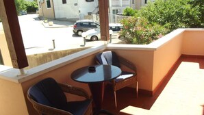 A balcony with wicker chairs and a small table, overlooking a street with parked cars and greenery. - Mediterraneo Goga Apartments - TwoBedroom Apartment With Terrace (Mali Losinj)