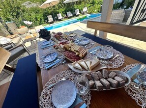 A poolside dining setup with a table set for a meal, surrounded by lounge chairs and umbrellas. - Three Bedroom Villa with Swimming Pool and Hot-Tub (Topolo)