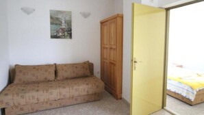 Een kleine kamer met een bank, een houten garderobe en een bed met een gele deken.