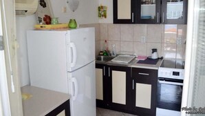 Een kleine keuken met een witte koelkast, een inbouwoven en donkere keukenkastjes.