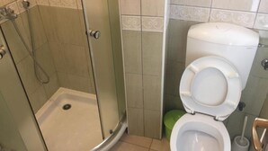 A bathroom with a glass-enclosed shower, a toilet, and a green trash bin. - Apartments Roza - Standard Double Room with Shared Bathroom 1 (Herceg Novi)