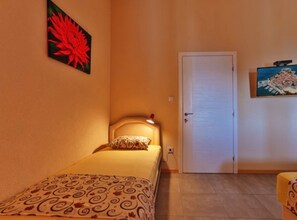 A small, single-bed room with a patterned bedspread, a bedside lamp, and a door to the right. - Studio Apartment with Sea View and Terrace (Sutomore)