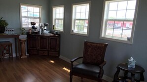 Une pièce avec un plancher en bois, une chaise en bois, une petite table avec une boîte de mouchoirs et une machine à café posée sur un comptoir.