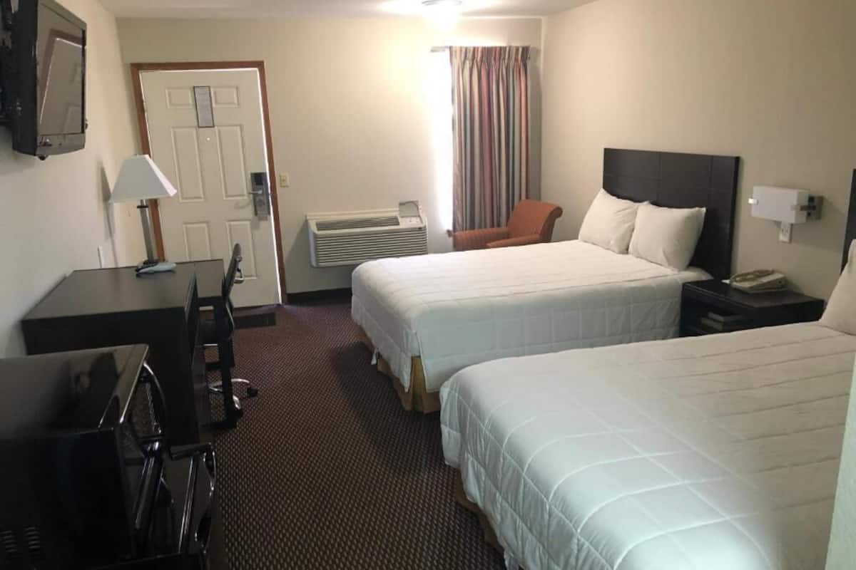 A hotel room with two beds, a desk with a chair, a TV, and a window with curtains.