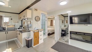 A modern kitchen with a microwave, sink, and cabinets, a small dining area, and a bedroom with a TV and a fireplace.