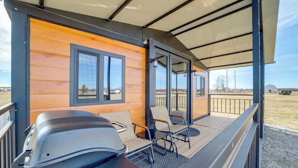 A covered outdoor seating area with a grill, chairs, and a view of the surrounding landscape.