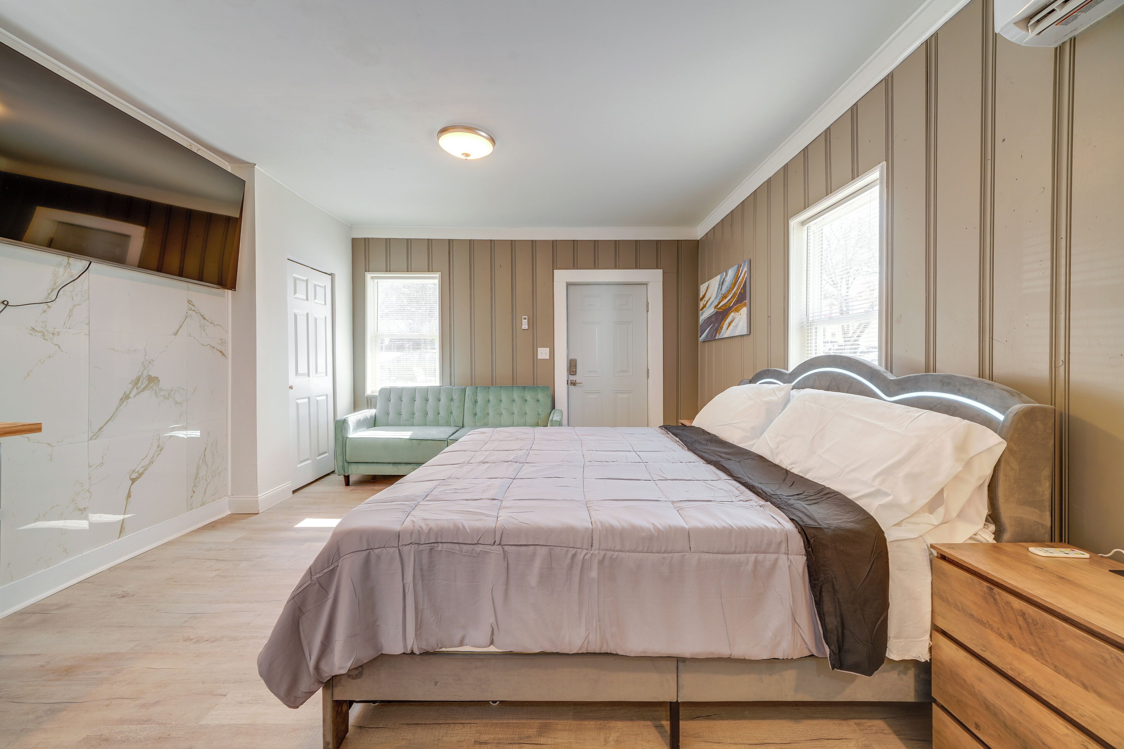 Une chambre à coucher avec un lit, une table de chevet en bois, un fauteuil vert et un mur en marbre.