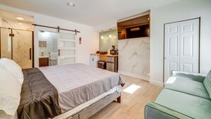 A modern bedroom with a bed, a green sofa, a bathroom with a shower, and a small kitchenette. - Explore the Hinton Historic District! Luxe Studio (Hinton)