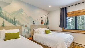 A hotel room with two beds, a mural of mountains, a window with a view of trees, and a cable car on the wall. - Luxe Mountain Home w/ Chef’s Kitchen & Okemo Views (Ludlow)
